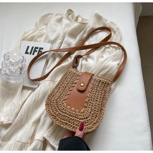 Détail d'un sac bandoulière en paille avec rabat en cuir marron sur tissu blanc