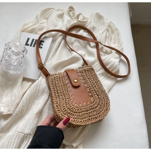 Détail du sac en paille avec rabat en cuir marron, fermoir métal et coutures soignées