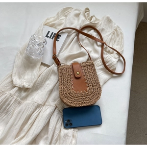 Détail du sac bandoulière en paille tressée avec lanière en cuir brun sur fond de robe
