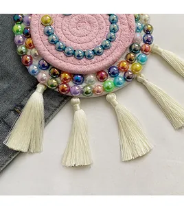 Macro shot of pink woven circular coaster with colorful beads and white tassels