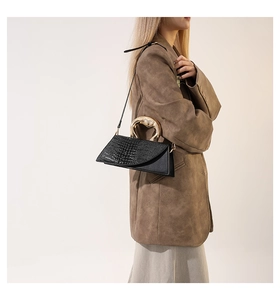 Détail du sac noir aspect croco avec poignée en métal doré et forme géométrique
