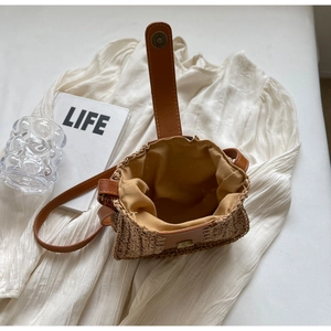 Gros plan du sac seau en paille avec fermeture magnétique et bandoulière en cuir marron