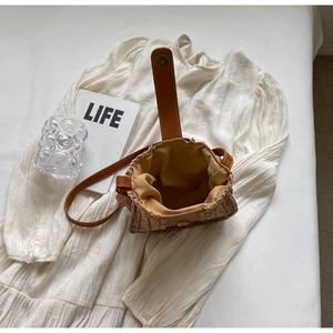 Détail du sac seau en paille avec bandoulière en cuir sur une robe d'été légère
