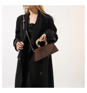 Détail d'un sac à main marron foncé à motif crocodile avec poignée en métal doré