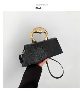Détail du sac à main noir avec poignée sculpturale dorée et texture cuir de crocodile