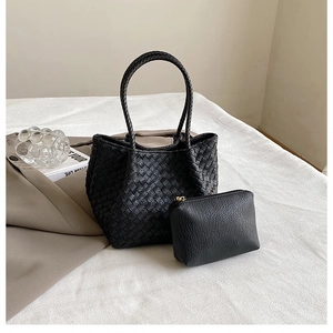 Detail of woven black tote bag with matching leather pouch on white textured fabric