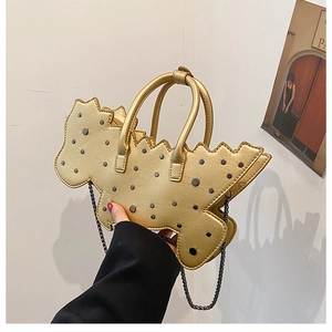 Detail of a golden cartoon-shaped handbag with metallic studs and a chain strap