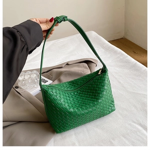 Detail of green woven crossbody bag featuring a golden zipper and knotted strap handle