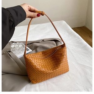Detail of hand-woven caramel leather texture and metal zipper on underarm bag