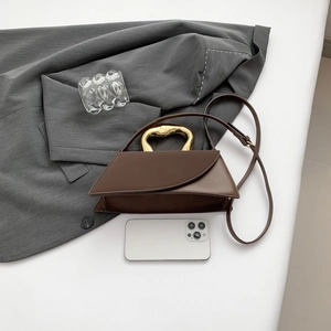 Modern brown leather crossbody bag with a unique gold metal handle and slim shoulder strap