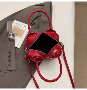Detail shot of a glossy red patent leather handbag with silver zipper on a gray blazer