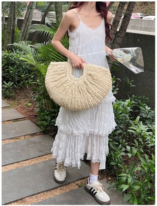 Outdoor lifestyle shot of a large beige straw handbag with textured woven patterns
