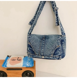 Detail of vintage acid wash denim crossbody bag featuring metal rivets and wide strap