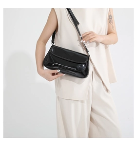Glossy black underarm bag with flap design shown on model in a minimalist style
