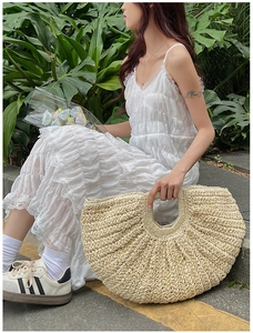 Detail of a beige woven straw handbag with a unique crescent shape and textured finish