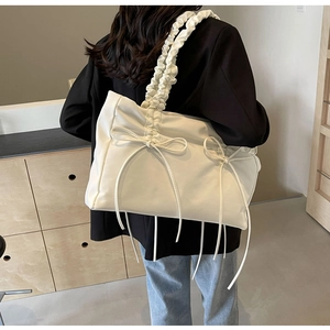 Detail van witte geplooide shopper met strikaccenten op model in zwarte blazer jas