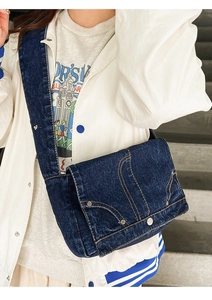 Detail of dark blue washed denim messenger bag with rivets worn by a model outdoors