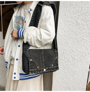Detail of vintage washed black denim messenger bag with contrast stitching and rivets