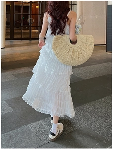 Rear view of a white lace tiered maxi dress paired with a large woven straw handbag