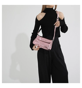 Detail of glossy pink patent leather baguette bag with adjustable strap worn by model