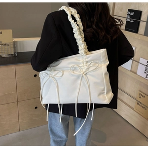 Detail van witte nylon schoudertas met strikjes en geplooide band gedragen door een model