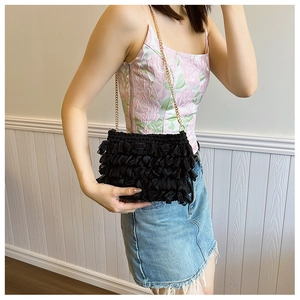 Detail of a black pleated chiffon crossbody bag with a delicate gold chain strap