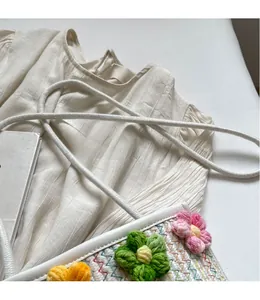 Detail of hand-woven white crossbody bag with colorful crochet flower patterns and long strap