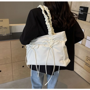 Detail van een witte tote bag met stijlvolle geplooide handvatten en strikjes met koord