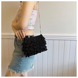 Detail of a black ruffled fabric crossbody bag with a delicate gold metal chain strap