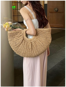Detailed view of large half-moon straw tote bag with woven texture carried by a model