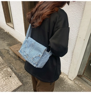 Detail of vintage blue denim messenger bag with pocket and button decor in street setting