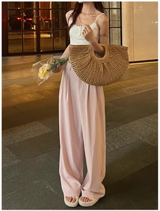 Detail of a khaki hand-woven straw bag paired with high-waisted pale pink trousers