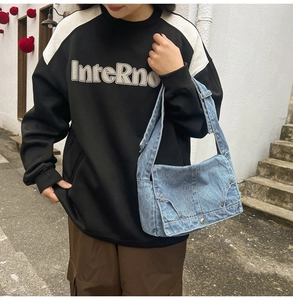 Detail of blue washed denim shoulder bag featuring high-quality stitching and metal snap button