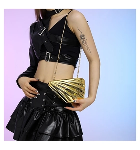 Close-up of shell-shaped gold metal clutch bag with chain strap held by a model