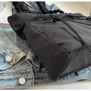Close-up van zwarte nylon tote bag met witte contraststiksels en gerimpeld wolkhandvat