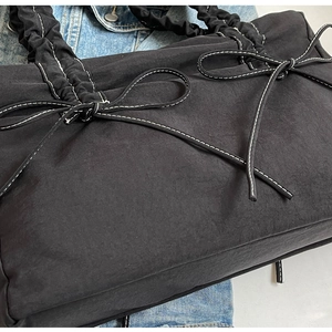 Detail van zwarte geplooide shopper met witte contraststiksels en een strikaccent