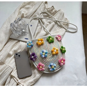 Detail shot of a white woven crossbody bag with colorful 3D crochet flower decorations