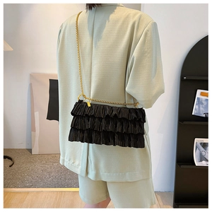 Detail of black tiered ruffle shoulder bag with gold chain strap on a green suit blazer