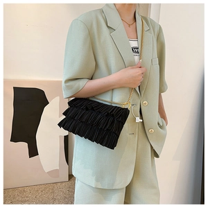 Detail of elegant black pleated fabric texture and delicate gold chain strap on shoulder bag