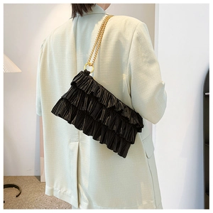 Detail of elegant black pleated ruffle handbag with gold chain on casual blazer