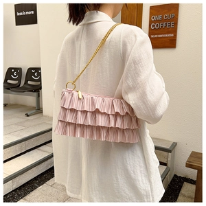 Detail of pink tiered ruffle shoulder bag with gold chain strap on model arm