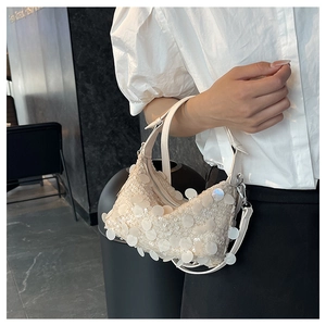 Close-up of cream sequin handbag showing textured wavy pattern and metallic zipper detail