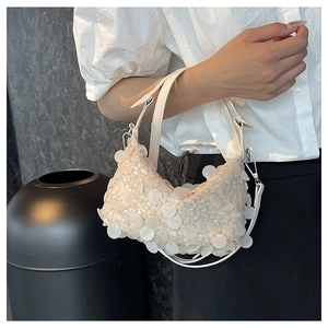 Close-up of white sequined crescent bag with shiny paillettes and metallic buckle details
