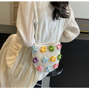 Detail of a handmade crochet crossbody bag with colorful floral patterns on white knit