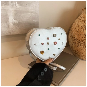Detail of silver heart-shaped crossbody bag with colorful gemstone studs and rivets