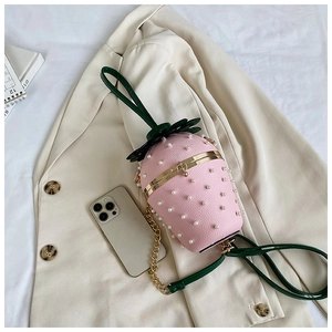 Macro detail of strawberry-shaped pink leather handbag with white pearl studs and chain