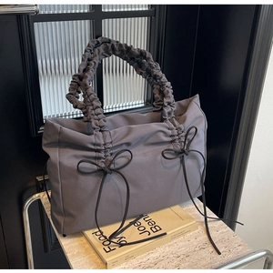 Detailweergave van het grijze geplooide handvat en decoratieve strikken op de tote bag