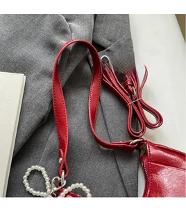 Detail of red leather shoulder bag strap featuring a white pearl bow charm ornament