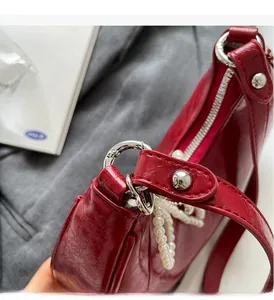 Close-up of dark red patent leather bag with silver buckle and pearl chain detail
