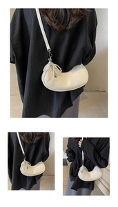 Detailed view of white half-moon bag featuring a pearl bow pendant and silver hardware